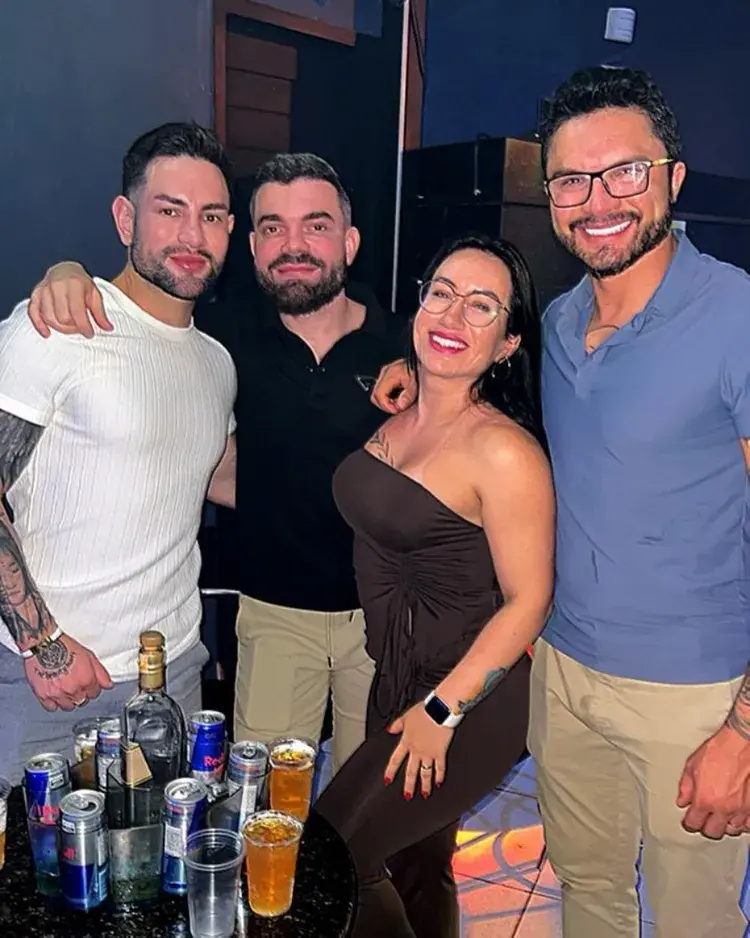 Quatro amigos se reunindo na boate DONANA PRIME, sorrindo e segurando bebidas, celebrando o sabadão. A imagem mostra um ambiente festivo.