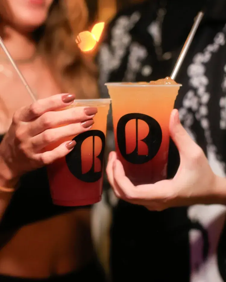 Duas pessoas brindando com drinks em copos do Rê, mostrando um ambiente festivo e acolhedor.