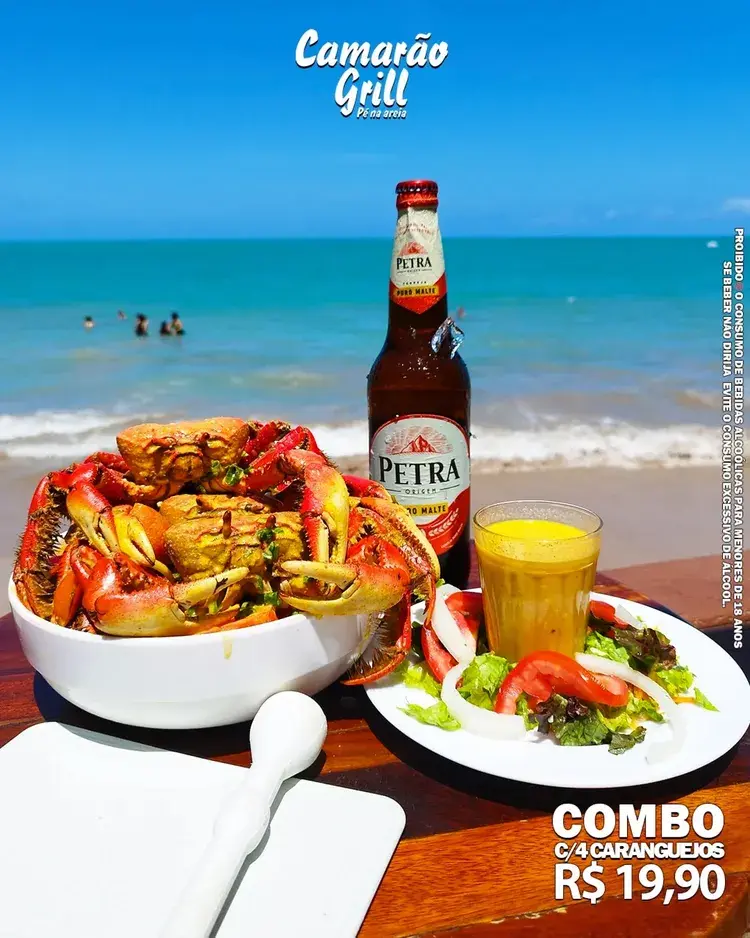 Imagem de um prato com caranguejos, uma cerveja Petra e um drink em um ambiente de praia, representando a promoção da Sexta do Caranguejo no Camarão Grill.