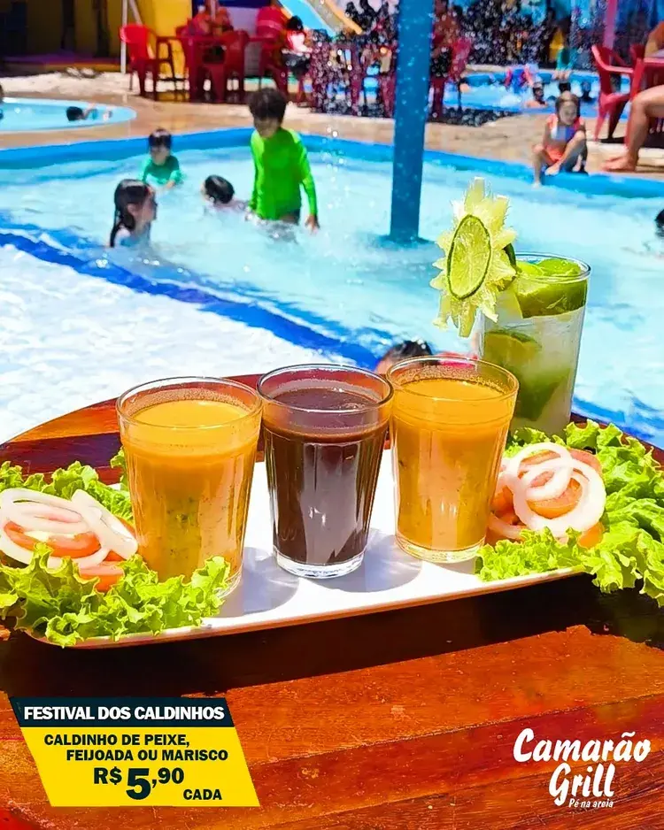 Imagem mostra três copos de caldinhos (peixe, feijoada e marisco) e um copo de caipirinha decorado, com piscina e crianças ao fundo, indicando ambiente de praia e lazer no Camarão Grill. Texto na imagem destaca "Festival dos Caldinhos" e preço de R$ 5,90 cada.