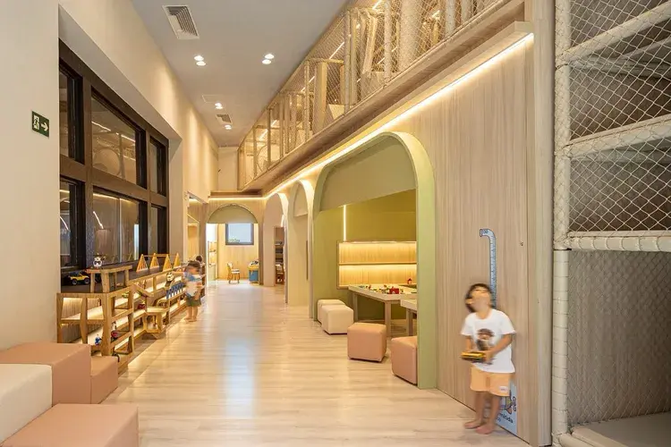 Imagem do Espaço Kids Camarões com crianças em brinquedoteca climatizada, ambientes de madeira clara e redes de proteção, localizado no Camarões Potiguar em Natal, com informações sobre valor e regras de acesso.