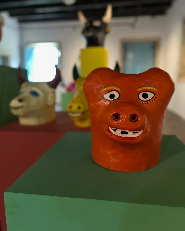 Imagem de uma escultura de máscara colorida em um espaço cultural, representando a exposição 'Desse e de Outros Carnavais - Ano III'.