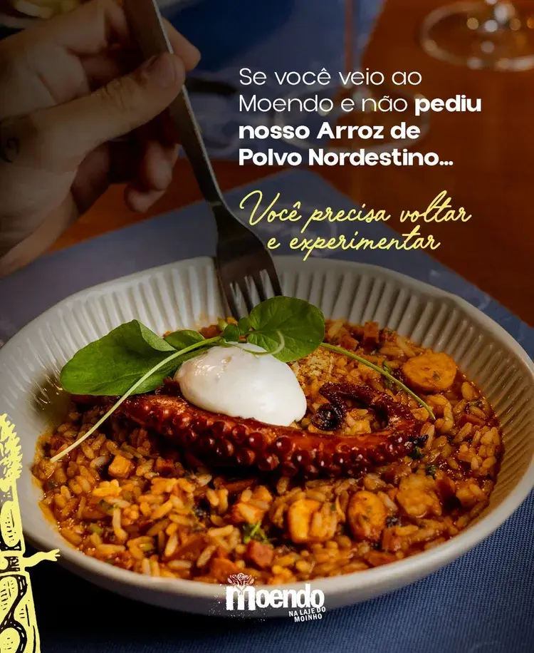 Prato de Arroz de Polvo Nordestino no Moendo. Apresenta arroz cozido em caldo de polvo e linguiça matuta, com uma cobertura de espuma de queijo e acompanhamentos em um ambiente acolhedor.