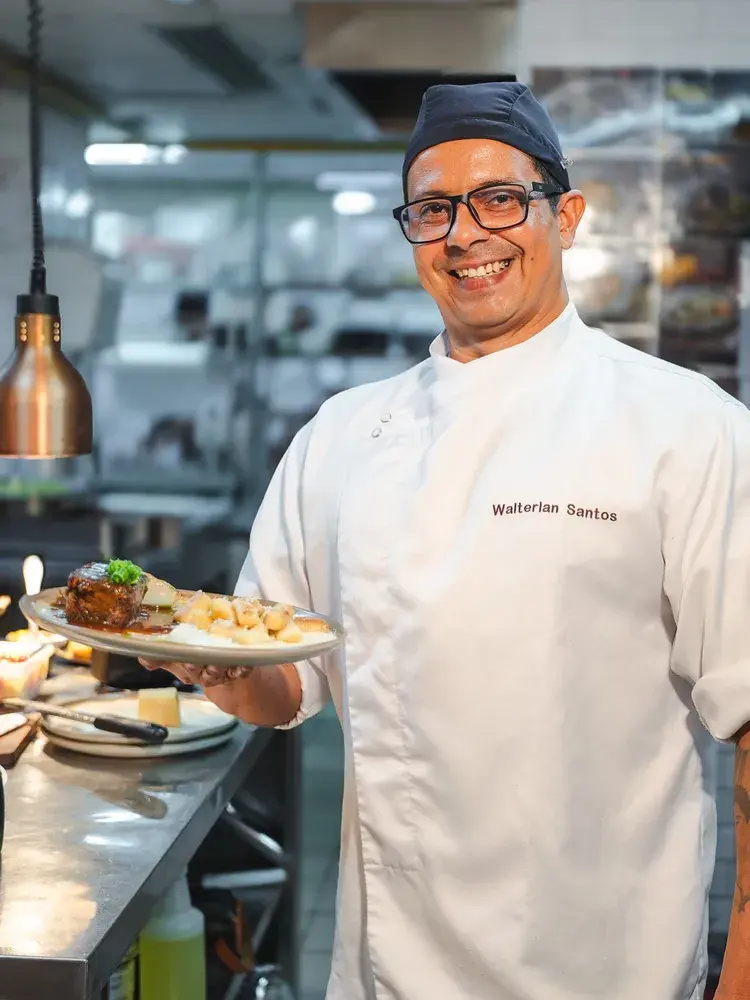 Chef Walterlan Santos segurando um prato com cupim e gnocchi no restaurante Santa Grelha, em João Pessoa.