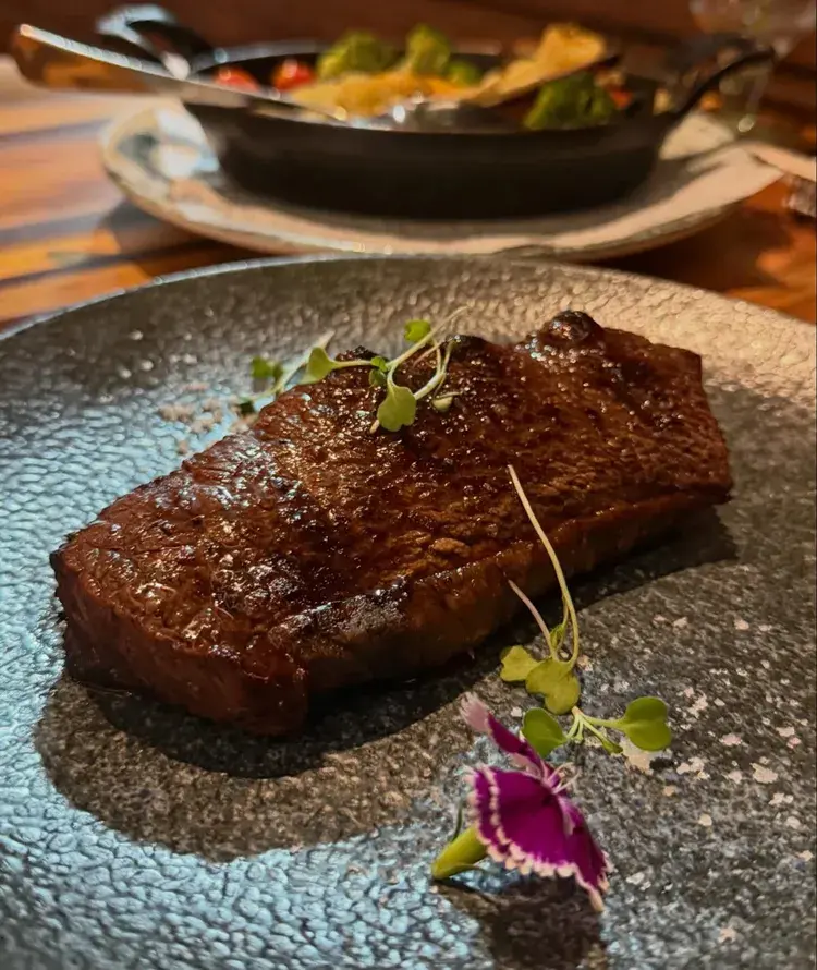 Imagem de um prato no NAU com picanha grelhada em fundo de mesa rústica; esta é uma das opções do Menu na BRASA, que inclui vários cortes e frutos do mar, disponível de 01 a 28 de fevereiro de 2026.