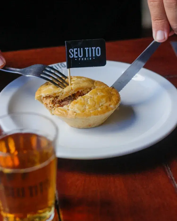 Imagem do Seu Tito apresentando um petisco com bebida.
