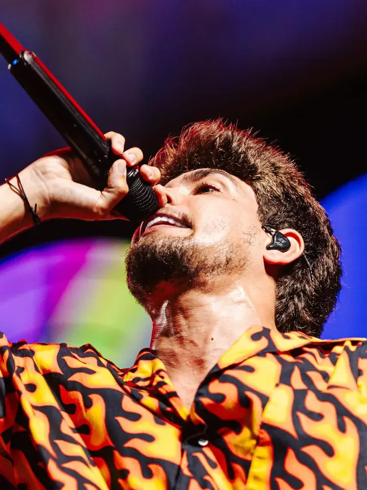 Imagem promocional colorida com o título Redação Praia, anúncio de vendas iniciadas para o verão 2026 em Pirangi, com datas 2 e 4 de janeiro e artistas listados. Inclui elementos gráficos de sol, mar, trompetistas e barcos.